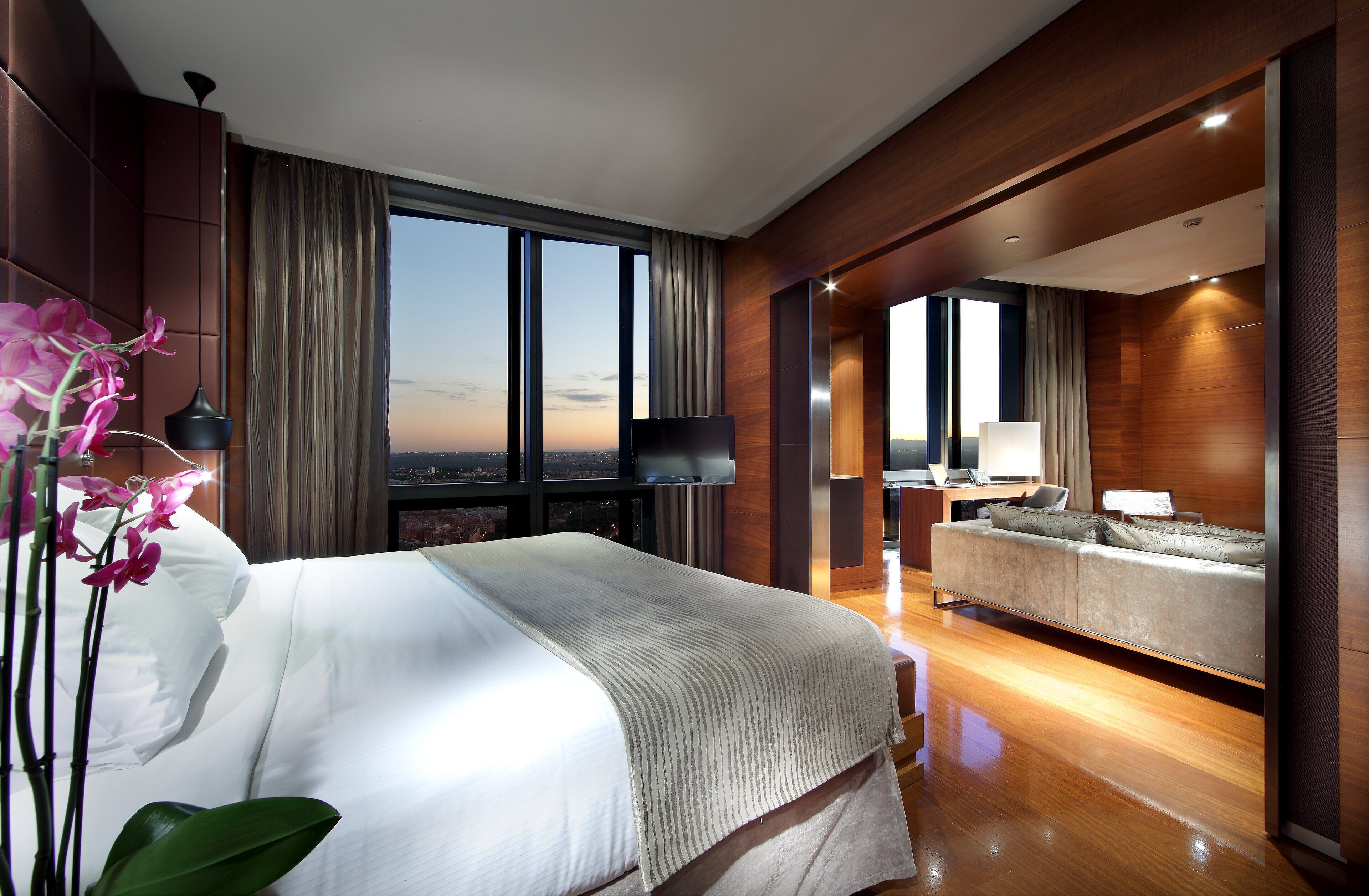 Habitación de hotel moderna con una cama grande, un sofá, un televisor y vistas a la ciudad.