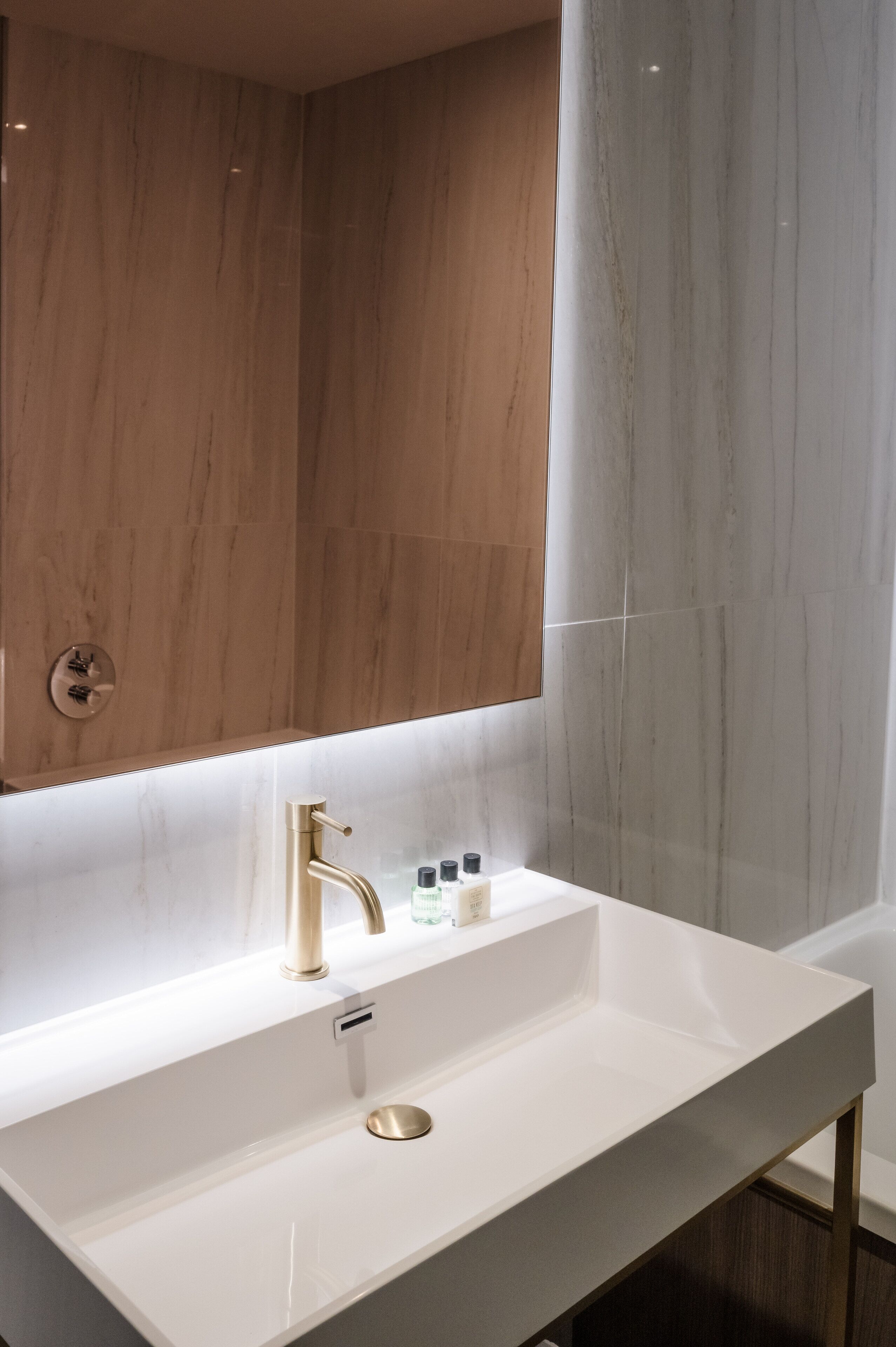 Un baño moderno con lavamanos blanco, grifo dorado y tocador de madera.