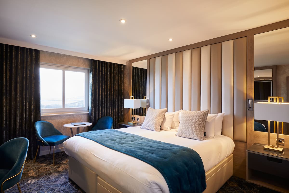 Une chambre d’hôtel avec un grand lit, un bureau, une chaise, une fenêtre et un miroir.