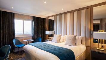 A hotel room with a large bed, a desk, a chair, a window, and a mirror.