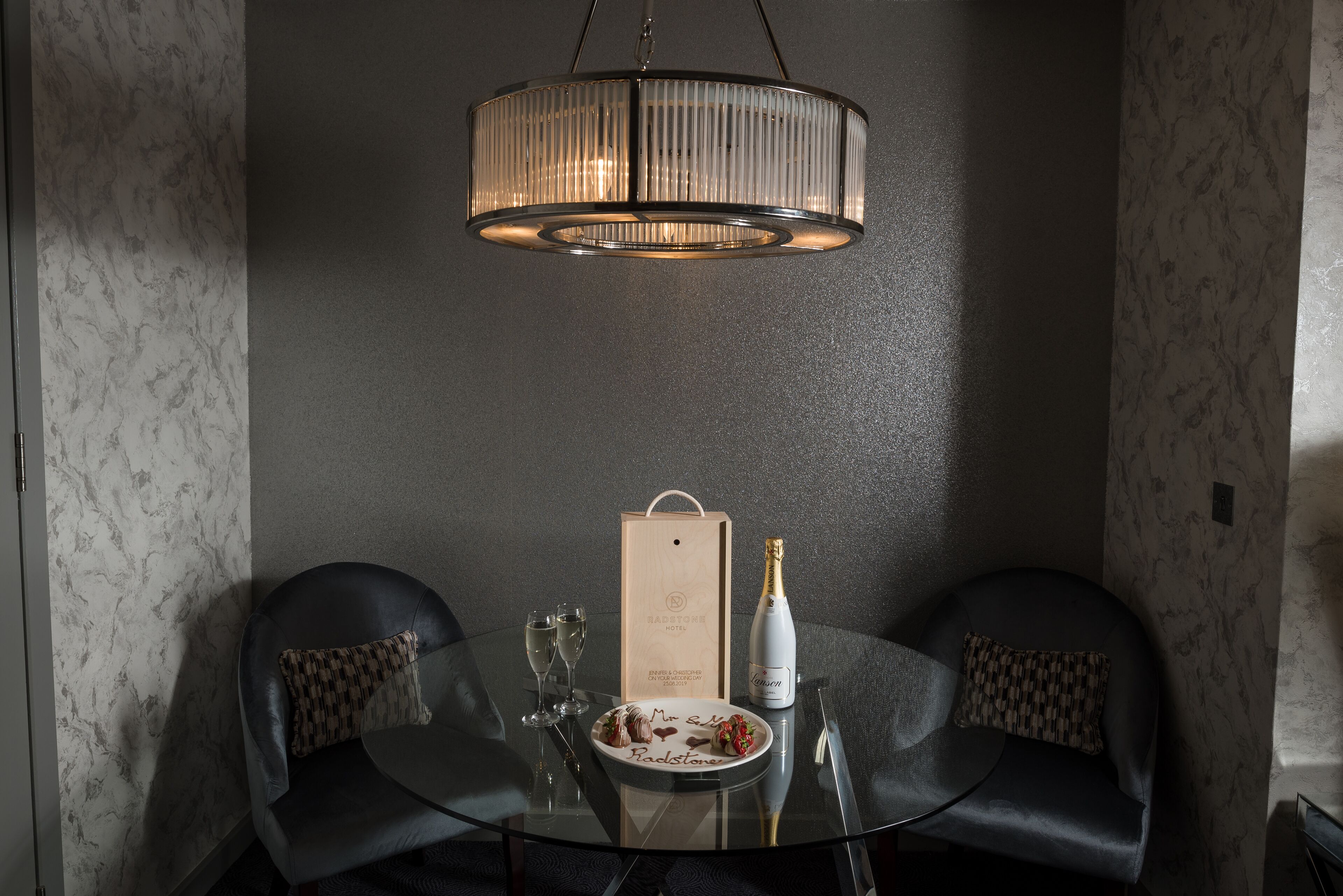 A dining table with a bottle of champagne, two glasses, and a plate of food.