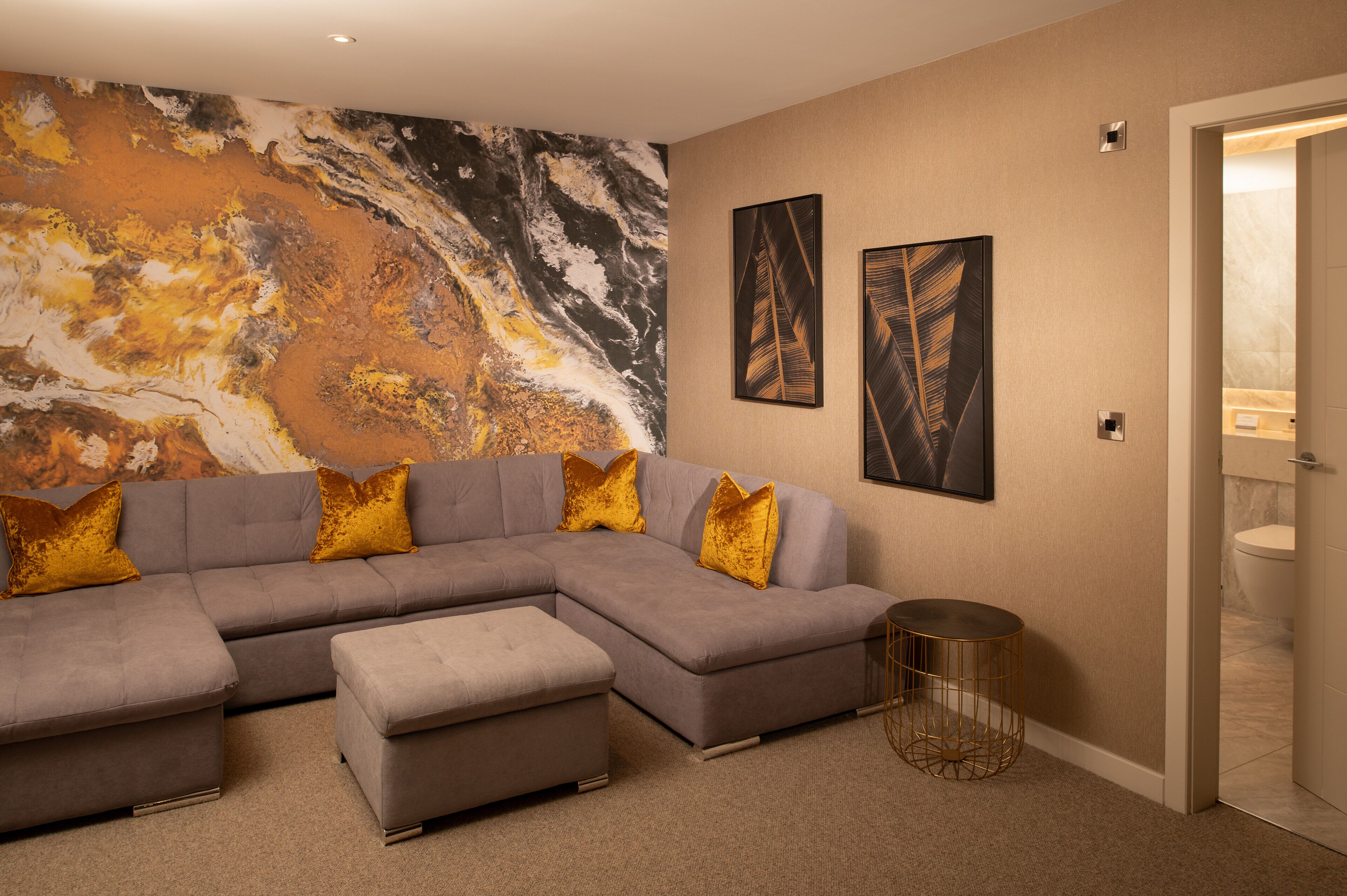 A modern living room with a sectional sofa, a round coffee table, and a large abstract mural on the wall.