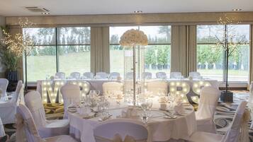 A banquet hall with round tables set for a formal event, large illuminated letters spelling "MRS" on the wall, and a decorative centerpiece.