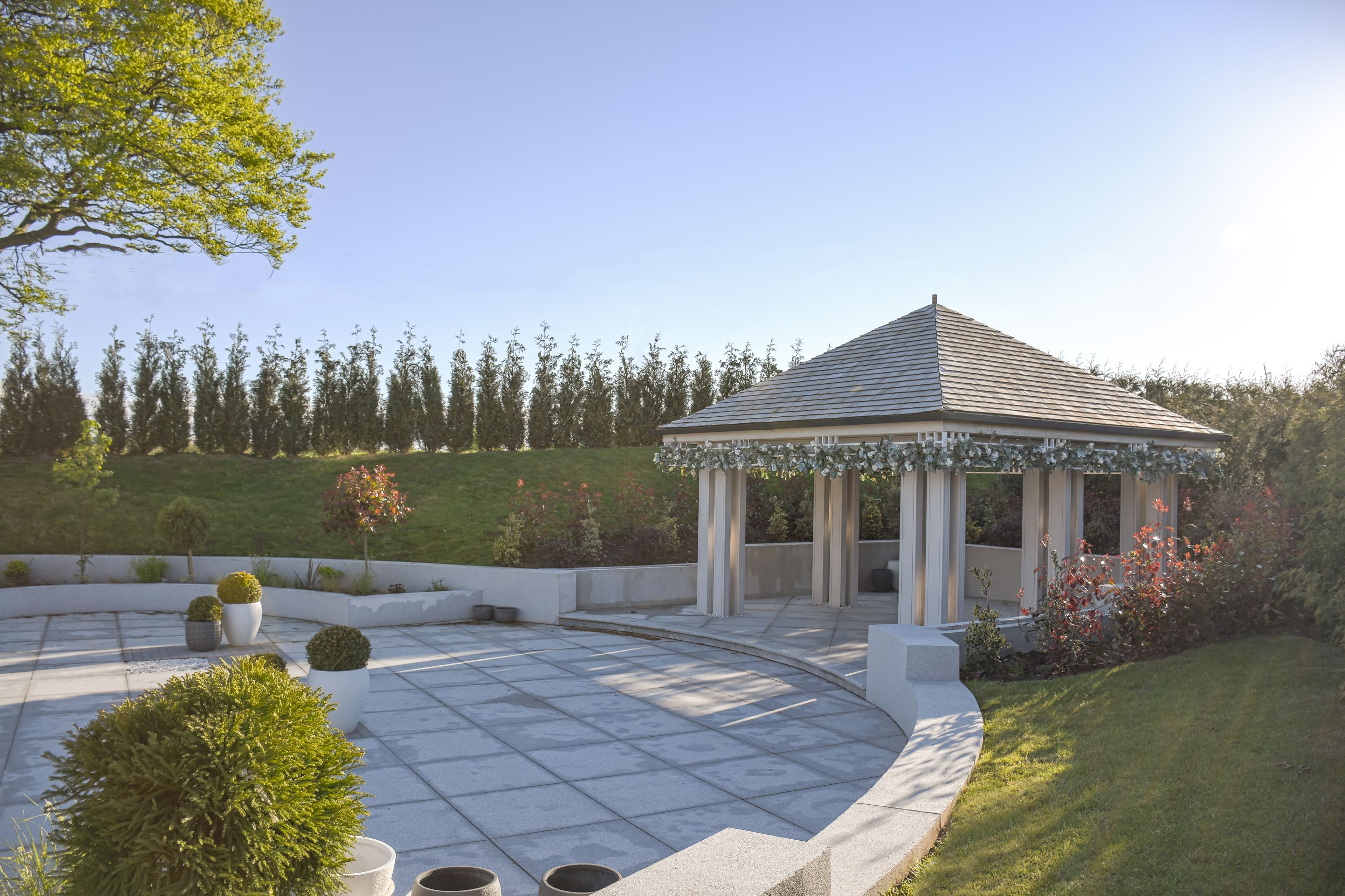 A gazebo with a tiled patio, surrounded by a landscaped garden with various shrubs and a lawn.