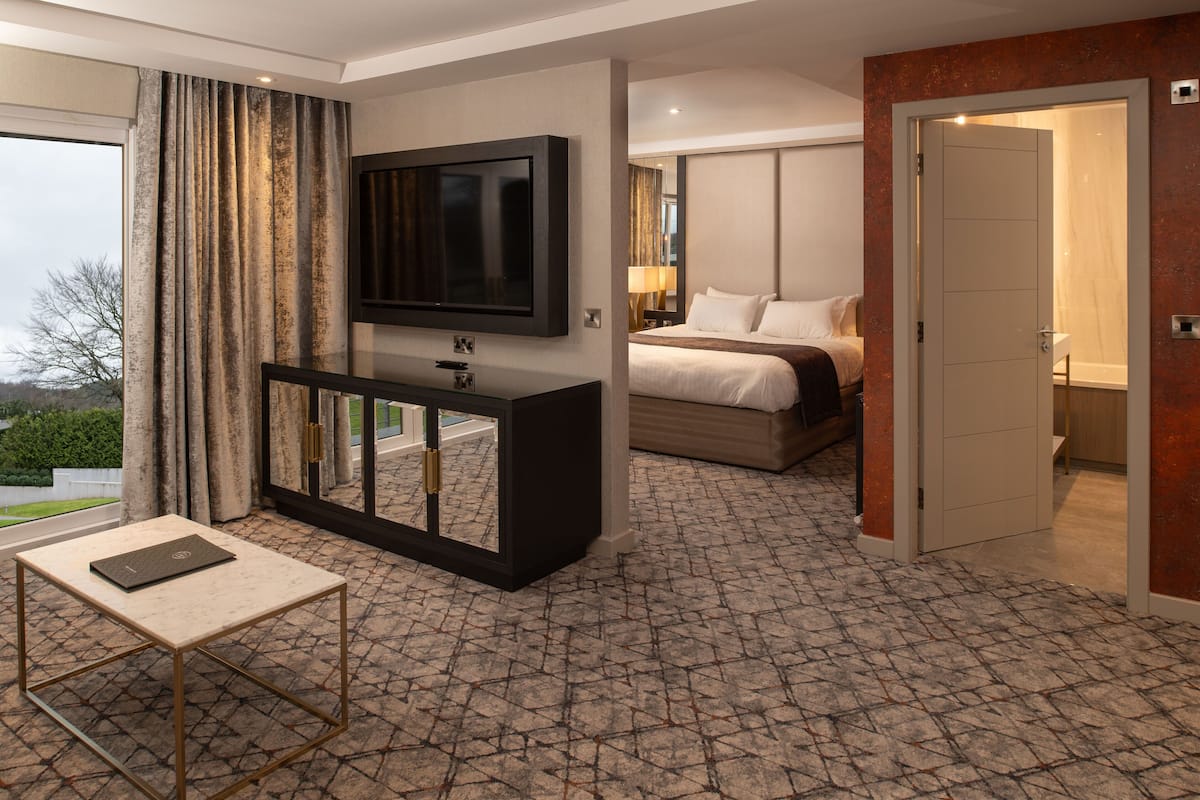 Une chambre d’hôtel avec un lit, un téléviseur fixé au mur, une petite table et une porte donnant sur une autre pièce.