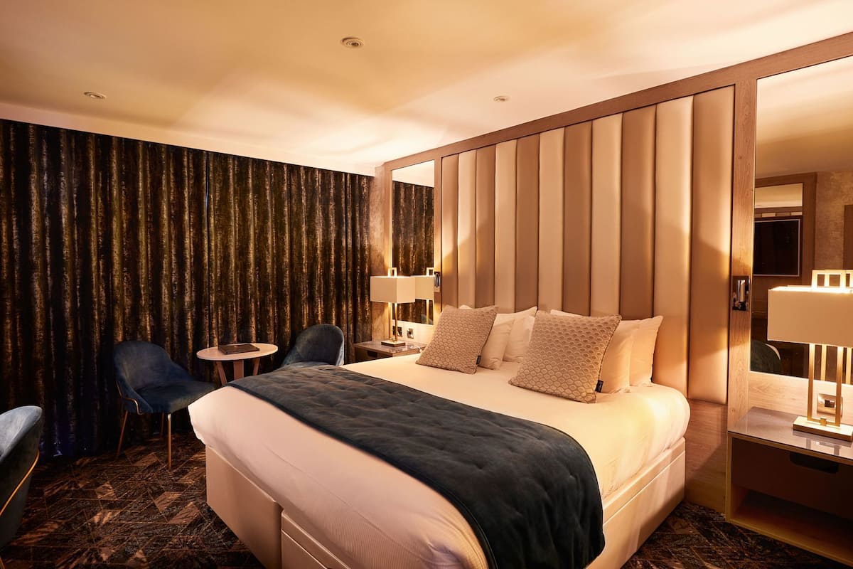 Une chambre d’hôtel avec un grand lit, un bureau, deux chaises, un miroir et un rideau.