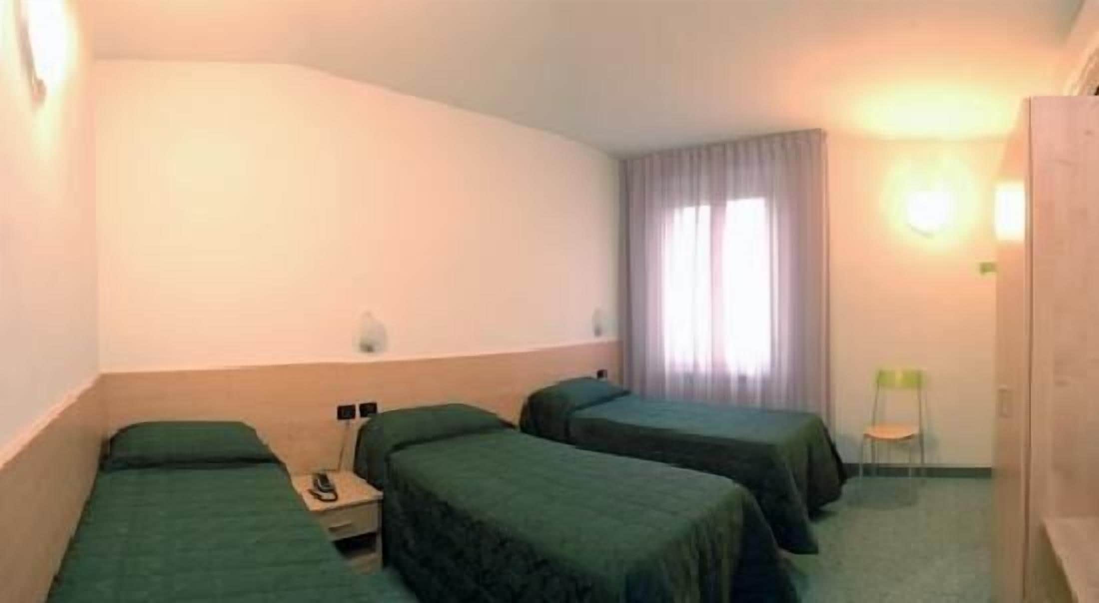 A hotel room with two single beds, a small bedside table with a phone, a nightstand, and a window with curtains.