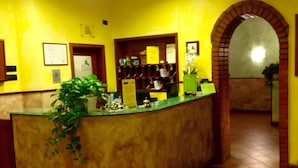A reception area with a marble counter, potted plants, and a brick archway. - Hotel Toscana (Prato)