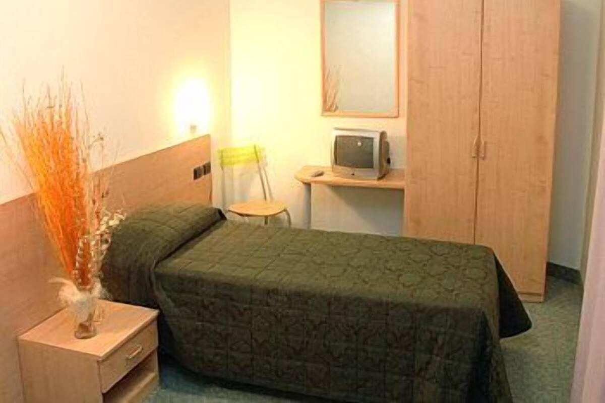 A hotel room with a bed, a desk with a computer, a chair, and a wardrobe.