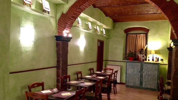 A dining area with wooden tables and chairs, a brick archway, and a counter with a lamp. - Hotel Toscana (Prato)