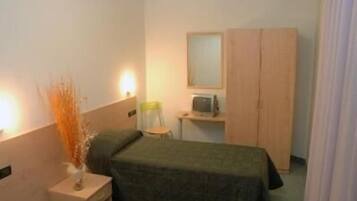 A small, simple hotel room with a single bed, a desk with a chair, a television, and a wardrobe.
