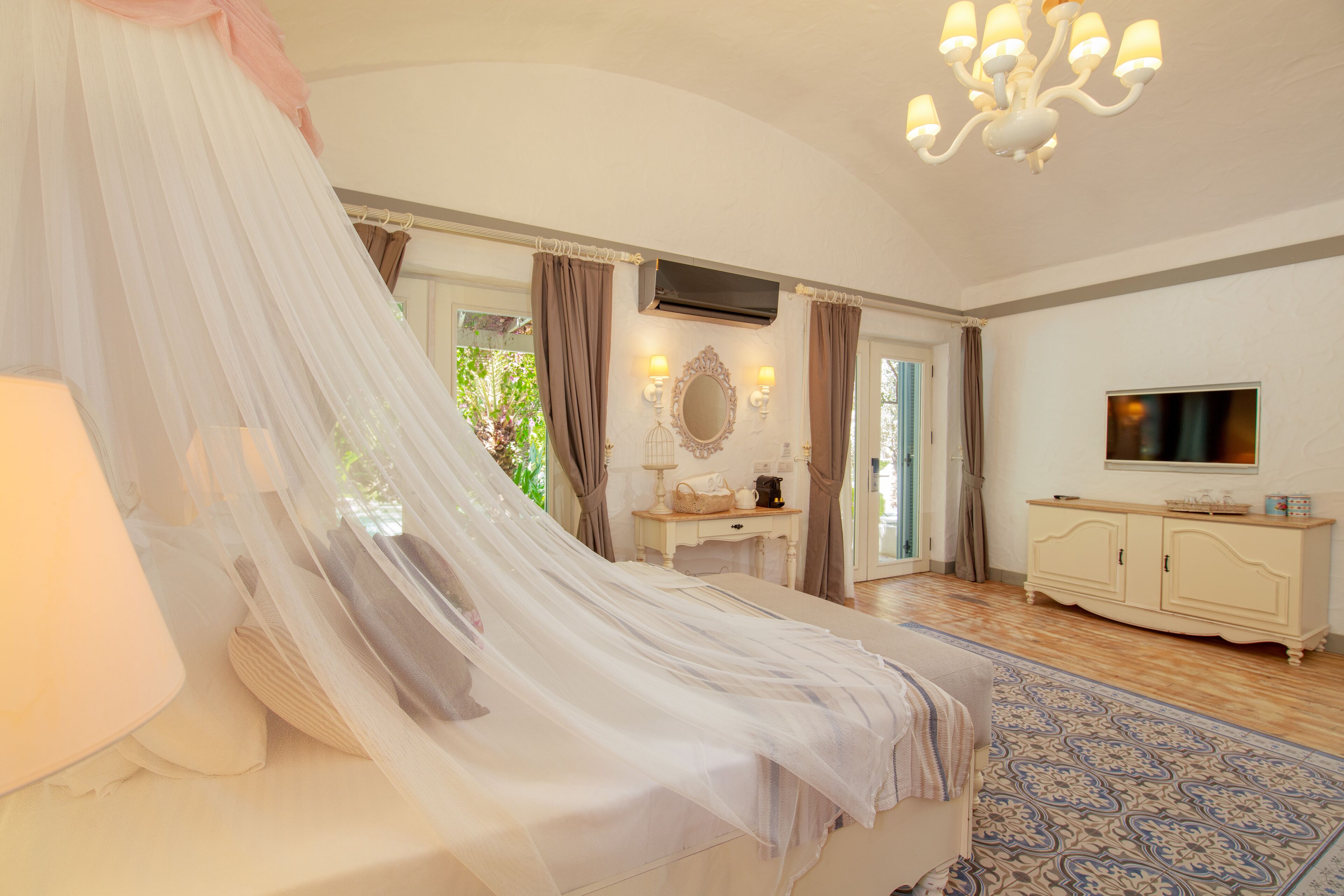 Un dormitorio con cama con dosel, tocador con espejo, televisor y alfombra estampada.