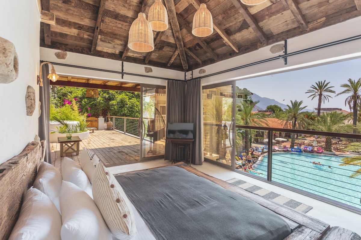 Un vaste balcon avec piscine, un plafond en bois et une vue sur les palmiers et les montagnes.