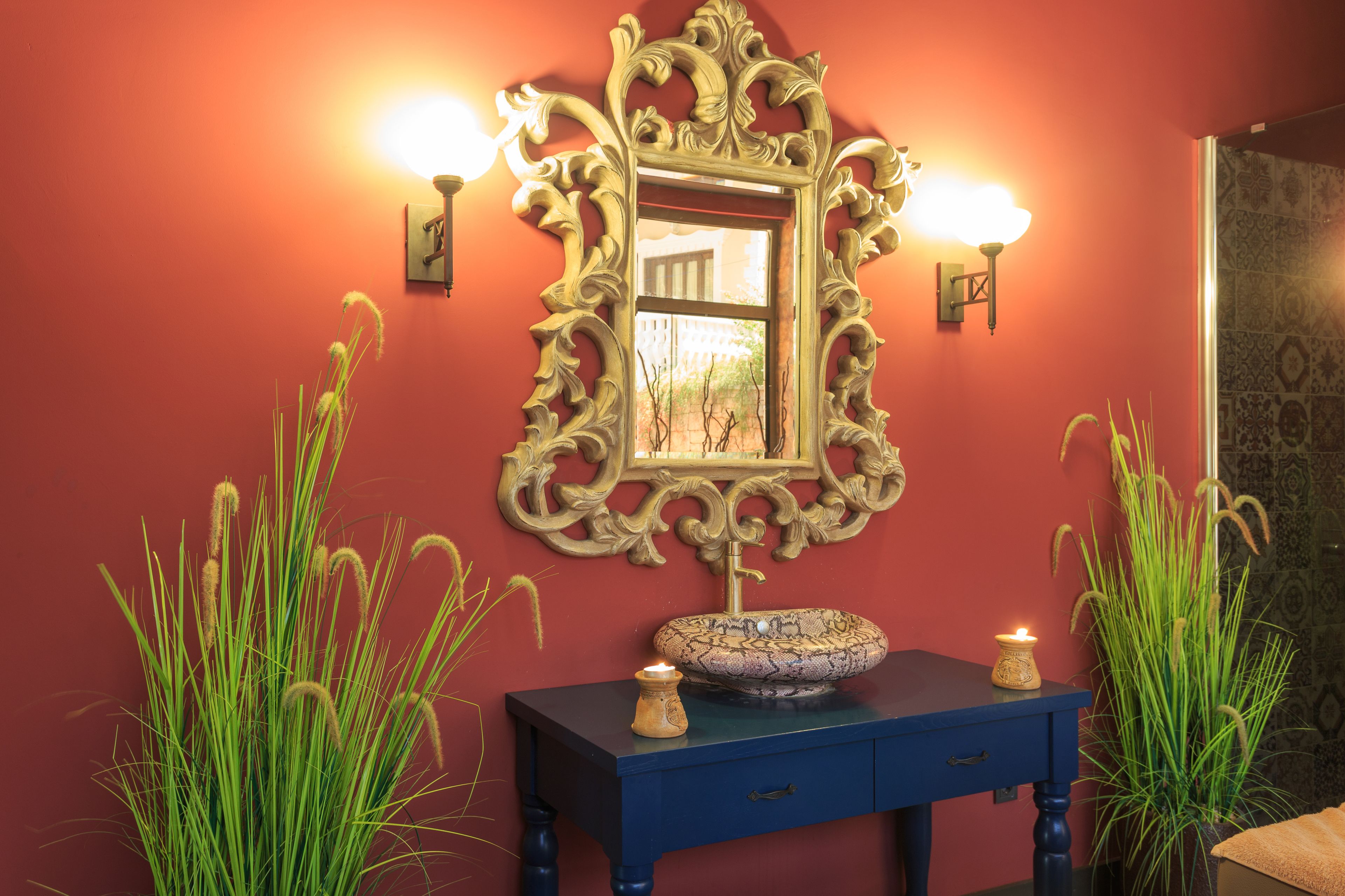 Une salle de bain agrémentée d’un miroir décoratif, d’appliques murales, d’un meuble-lavabo bleu et de hautes herbes.