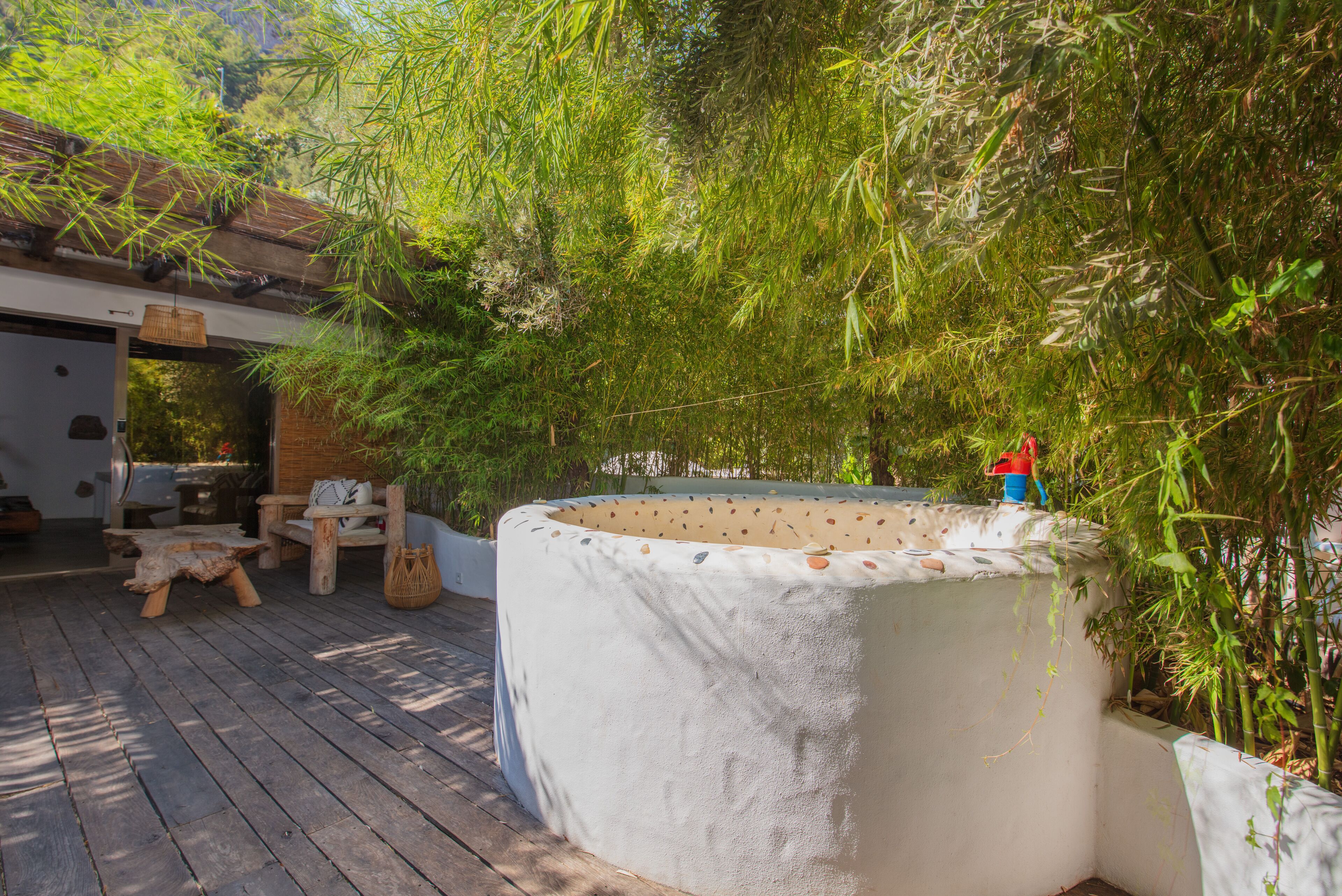 A wooden deck with a large, textured planter, outdoor furniture, and dense bamboo foliage.