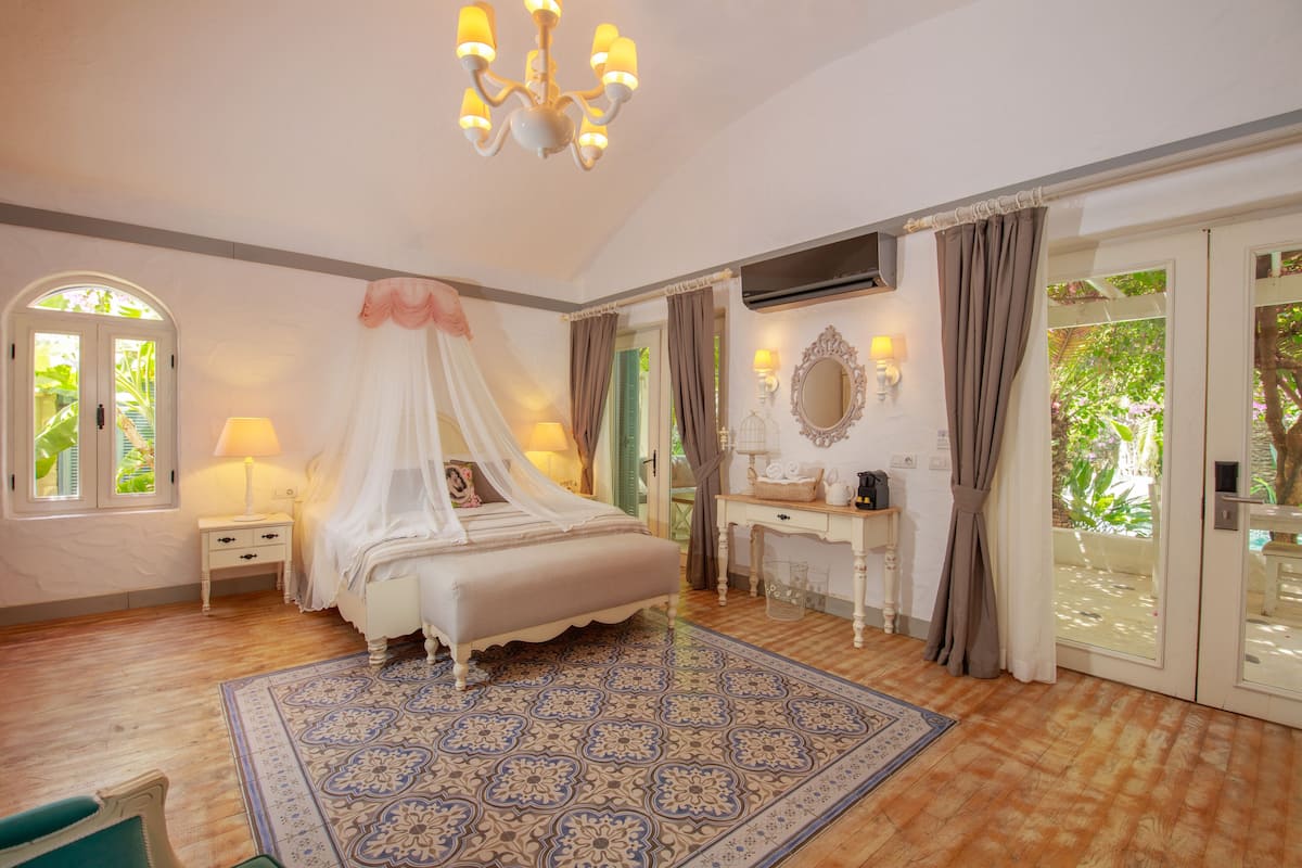 Une chambre à coucher avec un lit à baldaquin, une table de chevet avec une lampe, une coiffeuse et une grande fenêtre avec des rideaux.