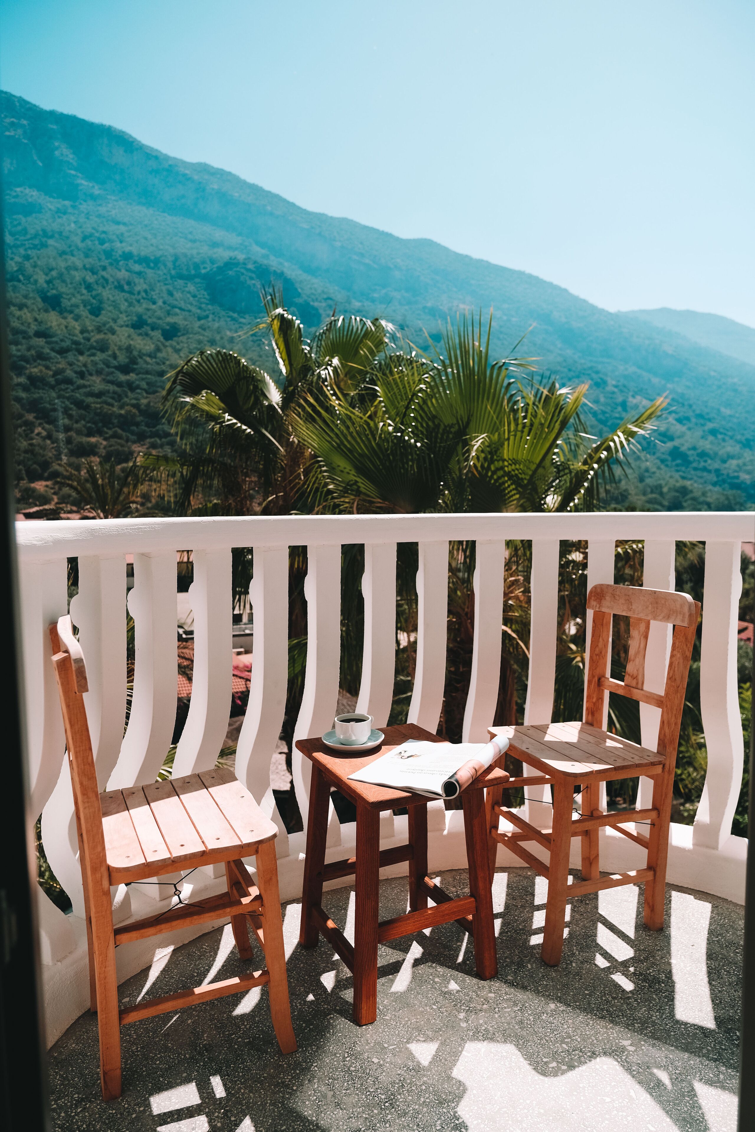 Een houten tafel met stoelen op een balkon, met uitzicht op groene bergen.