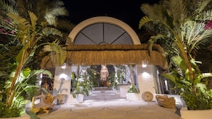 A tropical resort entrance with a thatched roof, potted plants, and a large circular window. - Flamingo Hotel & Spa - Pet Friendly (Fethiye)