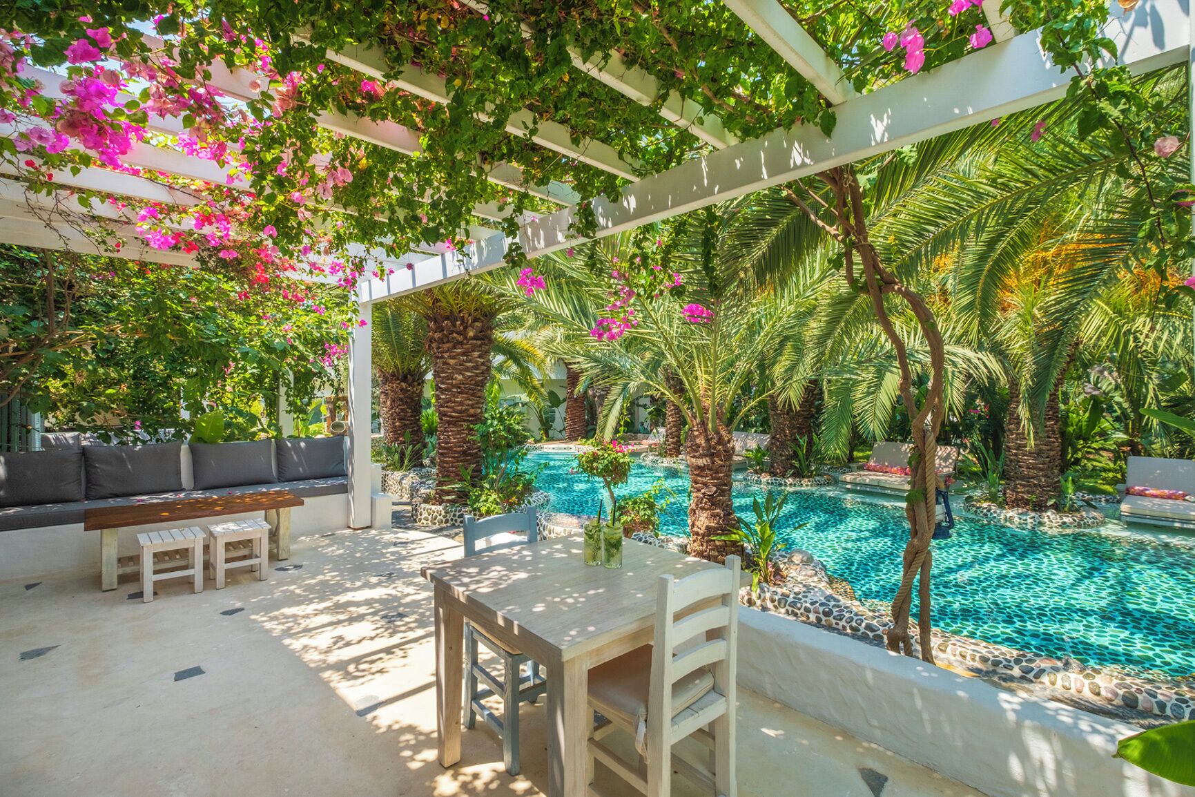 A poolside area with a pergola, seating, and palm trees.