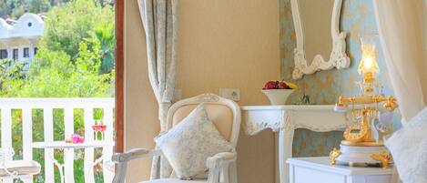 A room with a balcony, a white chair with a patterned pillow, a bedside table with a lamp, and a decorative mirror.
