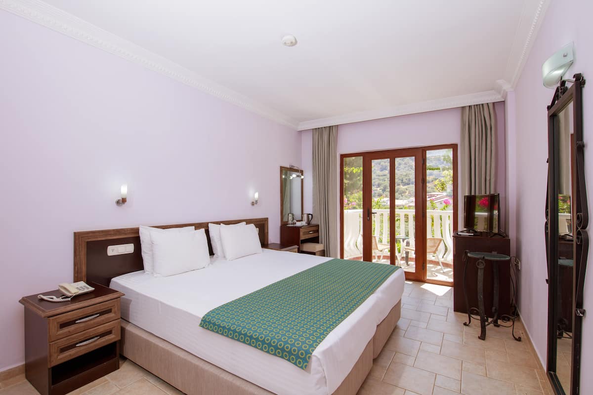 Une chambre d’hôtel avec un grand lit, une table de chevet avec un téléphone, un miroir et une vue sur le balcon extérieur.