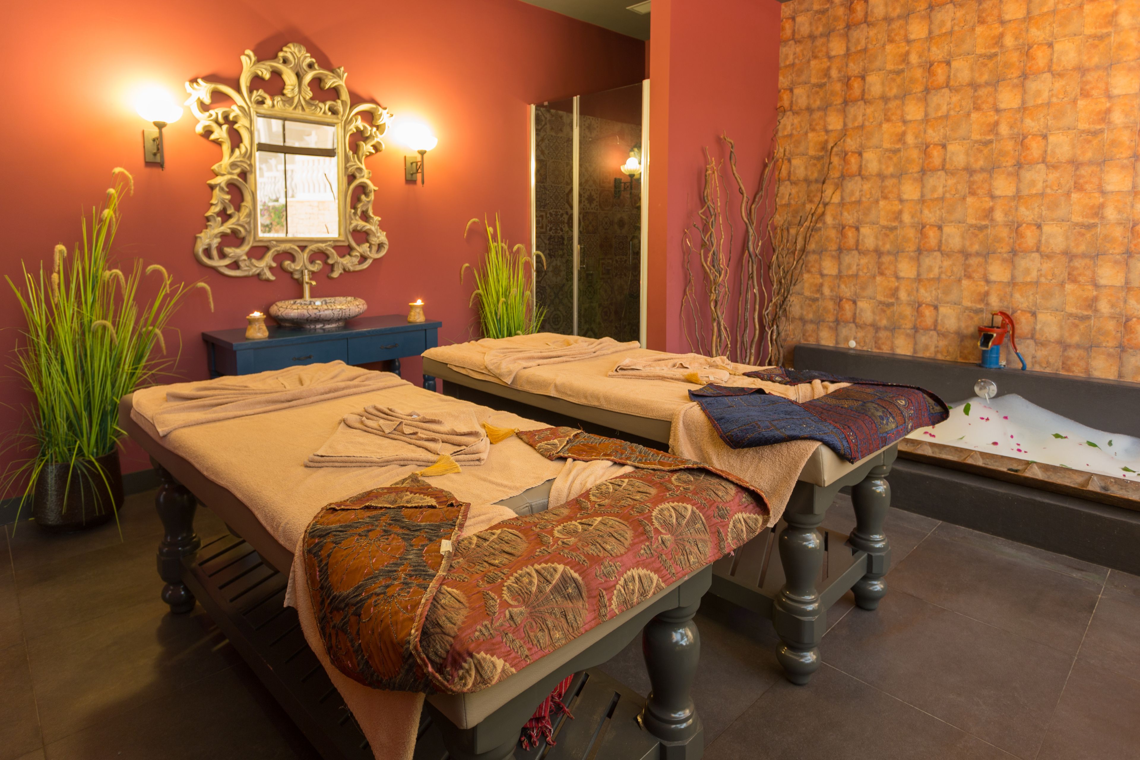 A spa room with two beds, a mirror, wall sconces, a small table, and a decorative wall.