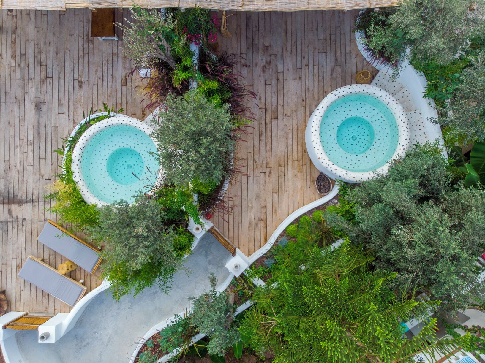 A rooftop pool area with two circular pools surrounded by lush greenery and wooden decking.