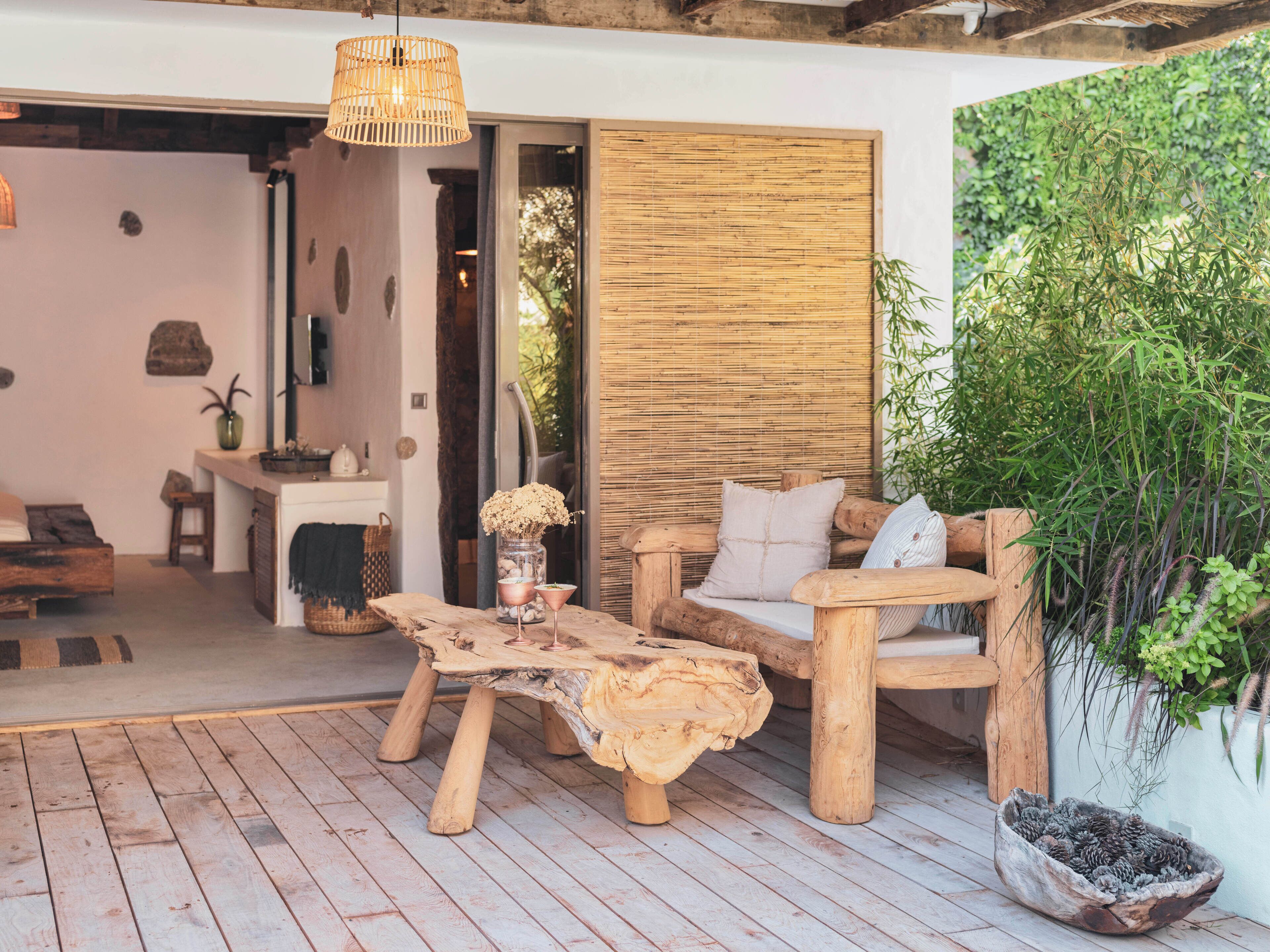 A rustic wooden outdoor seating area with a woven table and chairs, a hanging light fixture, and a bamboo wall.