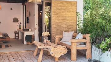 A rustic wooden outdoor seating area with a woven table and chairs, a hanging light fixture, and a bamboo wall.