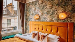 A bedroom with a large bed, a green upholstered bench, a rustic wall, and a window with curtains. - Atholl Arms Hotel (Dunkeld)