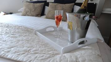 A bed with a white quilt, a champagne bottle in a metal bucket, and a glass of champagne on a tray.