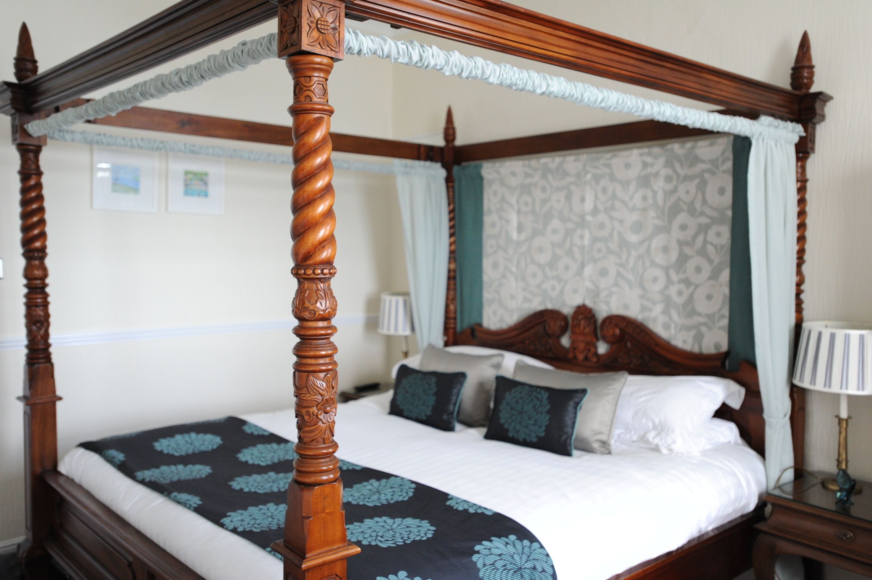 Una cama con dosel con un edredón estampado con motivos florales, un cabecero de madera y una mesita de noche con una lámpara.