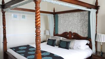 Una cama con dosel con un edredón estampado con motivos florales, un cabecero de madera y una mesita de noche con una lámpara.