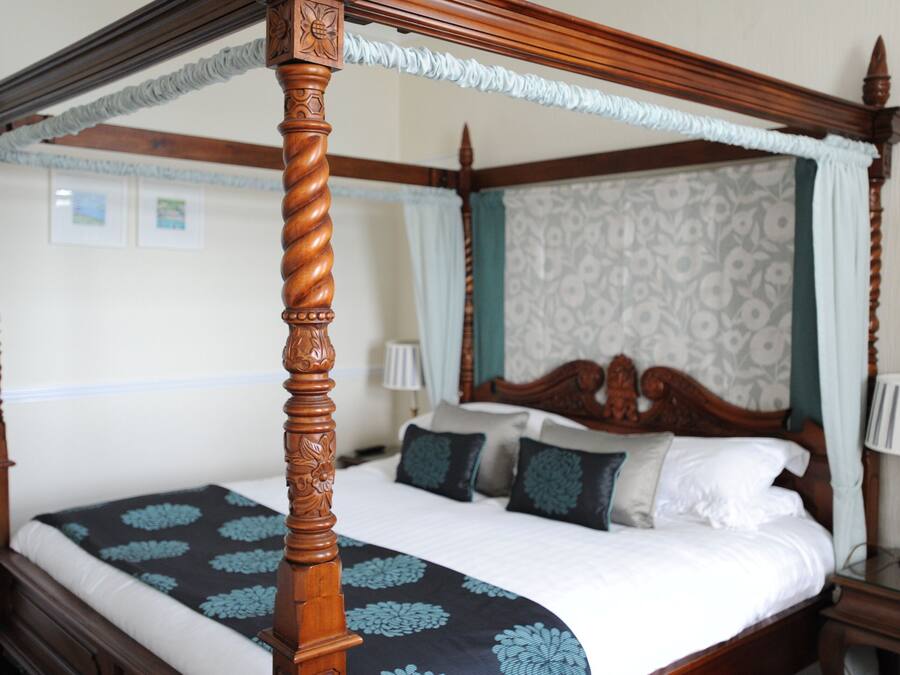 Una cama con dosel con un edredón estampado con motivos florales, un cabecero de madera y una mesita de noche con una lámpara.