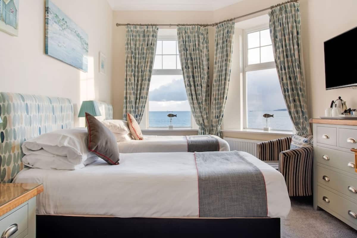 A bedroom with two beds, a view of the sea, a TV, and a dresser.