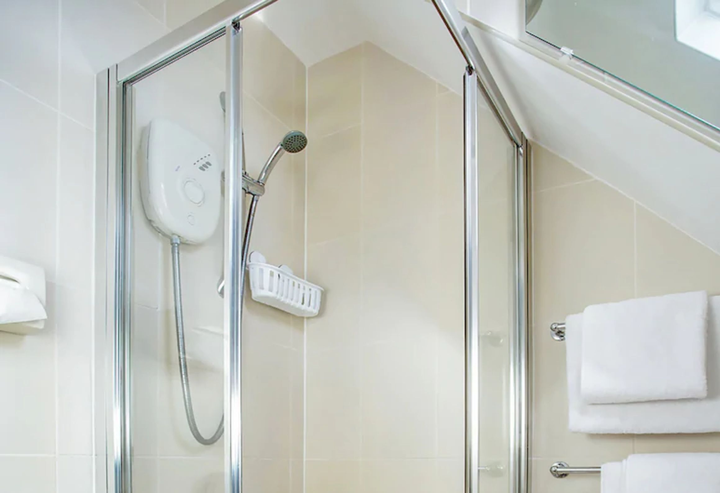A glass-enclosed shower with a handheld showerhead and a wall-mounted control panel.