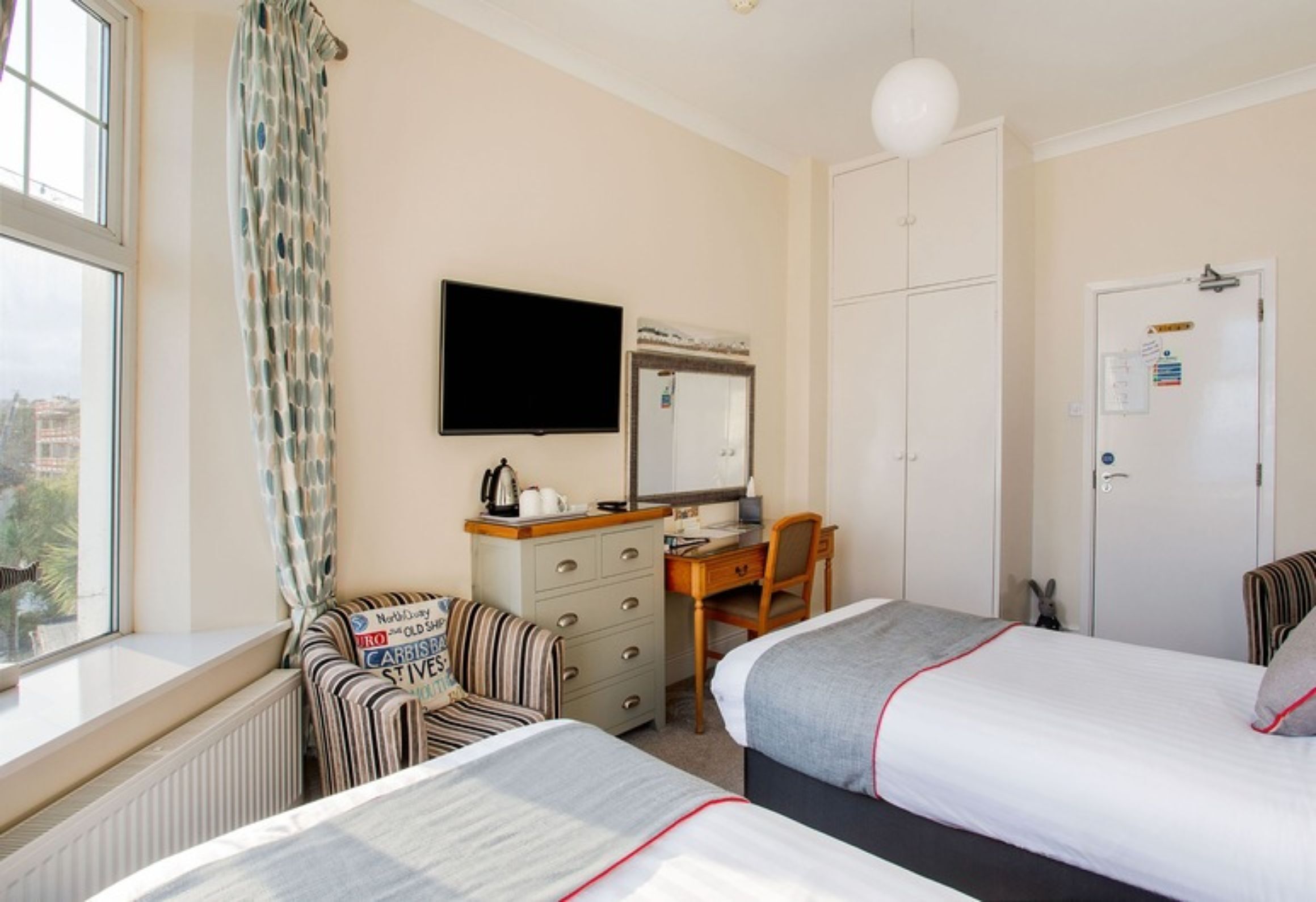 A hotel room with two beds, a desk, a chair, a television, and a window with curtains.