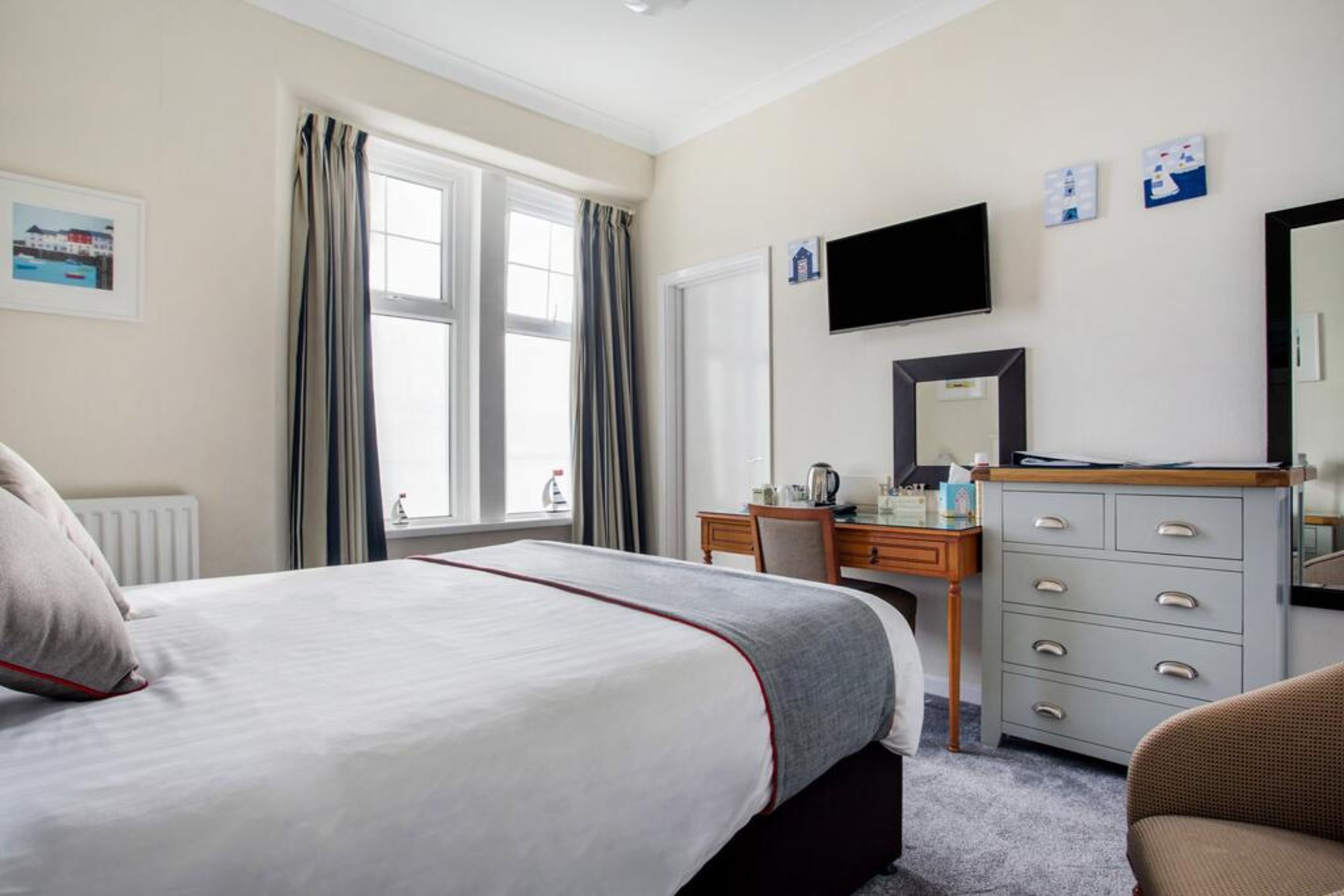 Habitación de hotel con cama, escritorio, silla, cómoda, televisor y ventana con cortinas.