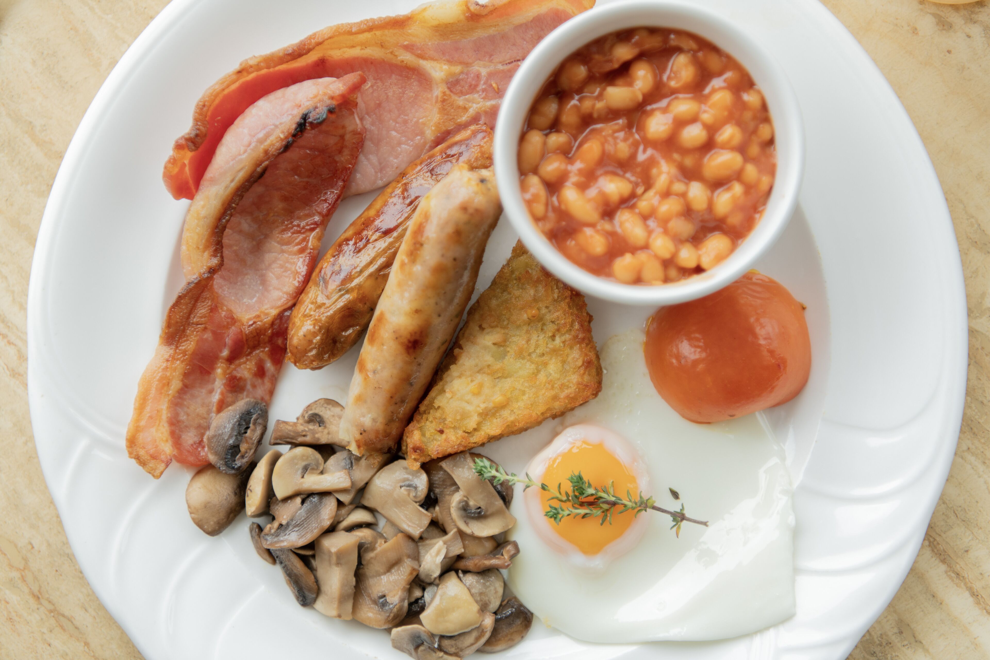 Un plato de desayuno con tocino, salchichas, champiñones, tostadas, frijoles, un tomate y un huevo escalfado.