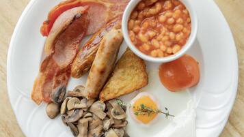Un plato de desayuno con tocino, salchichas, champiñones, tostadas, frijoles, un tomate y un huevo escalfado.