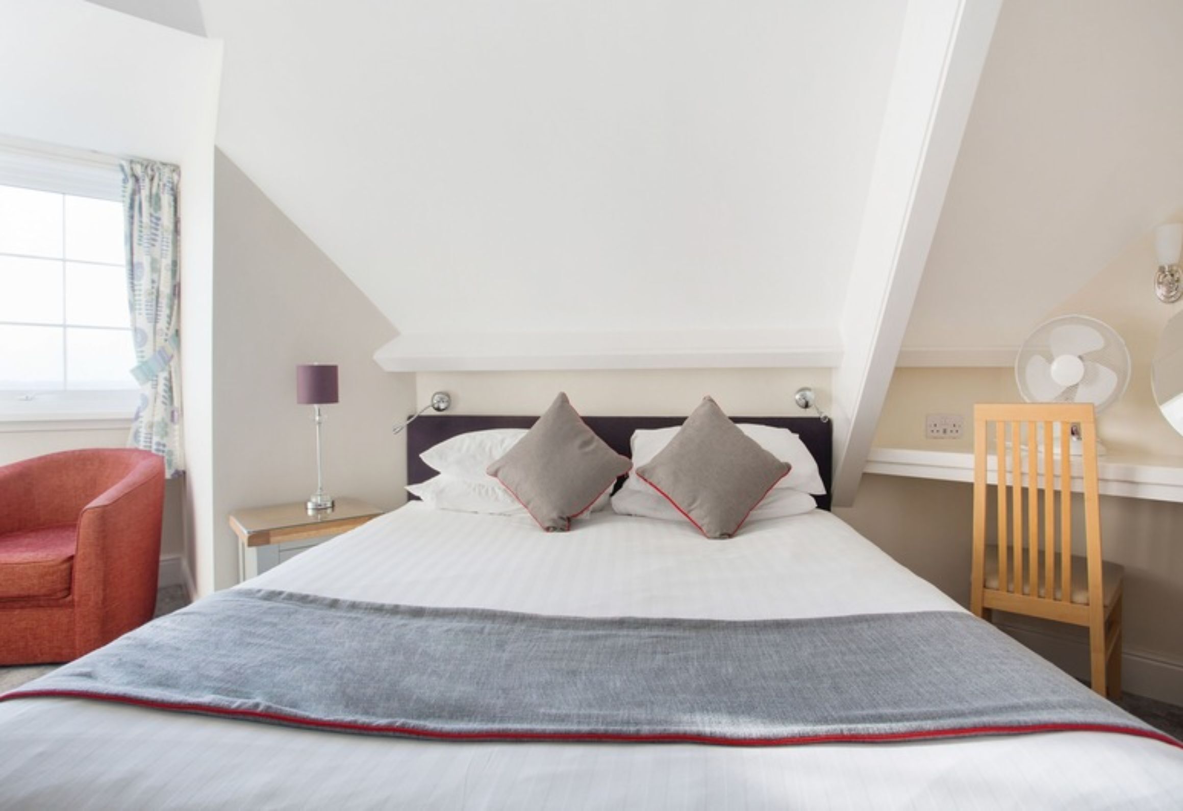 A bedroom with a bed, a chair, a desk, and a window with curtains.