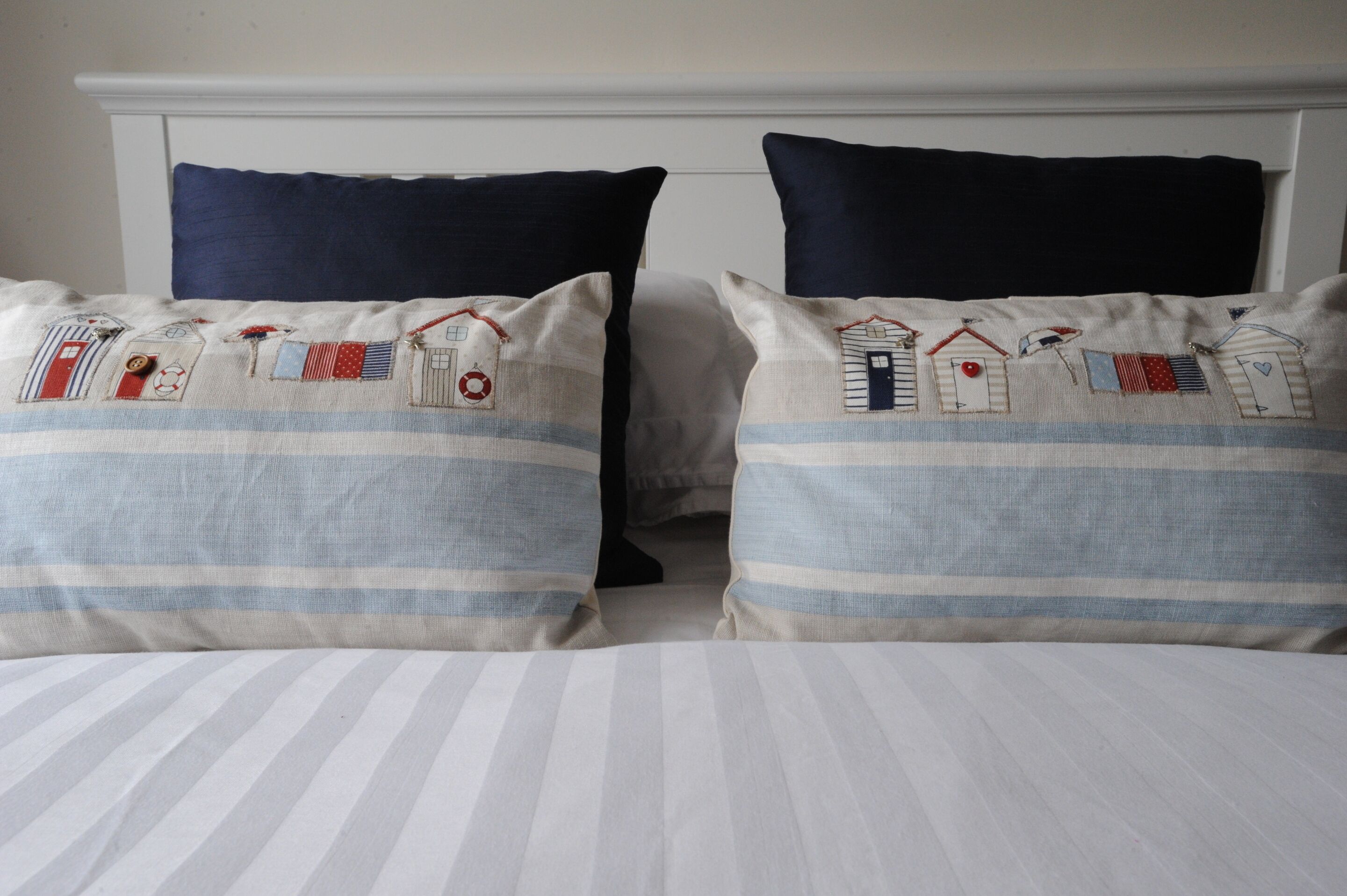 A bed with striped bedding and two pillows with nautical-themed embroidery.