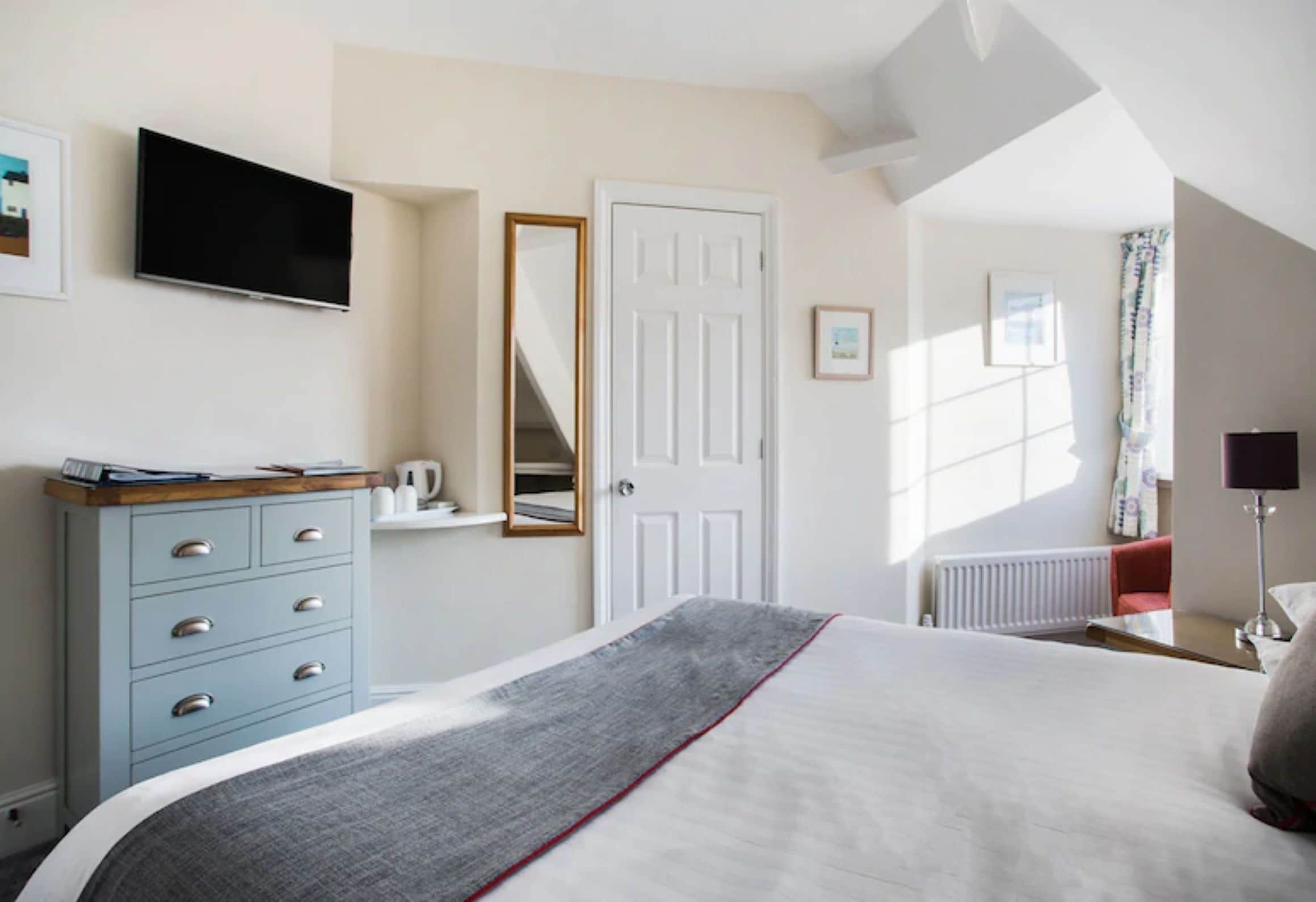 Une chambre à coucher avec un lit, une commode, un téléviseur, une porte et une fenêtre avec des rideaux.
