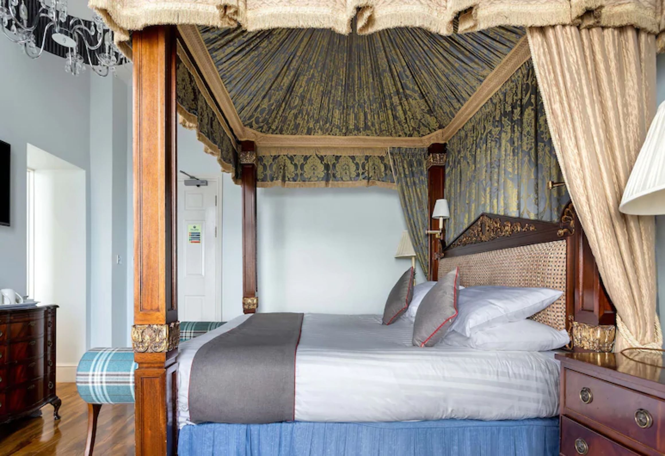 A four-poster canopy bed with a headboard, a bedside table, and a lamp.