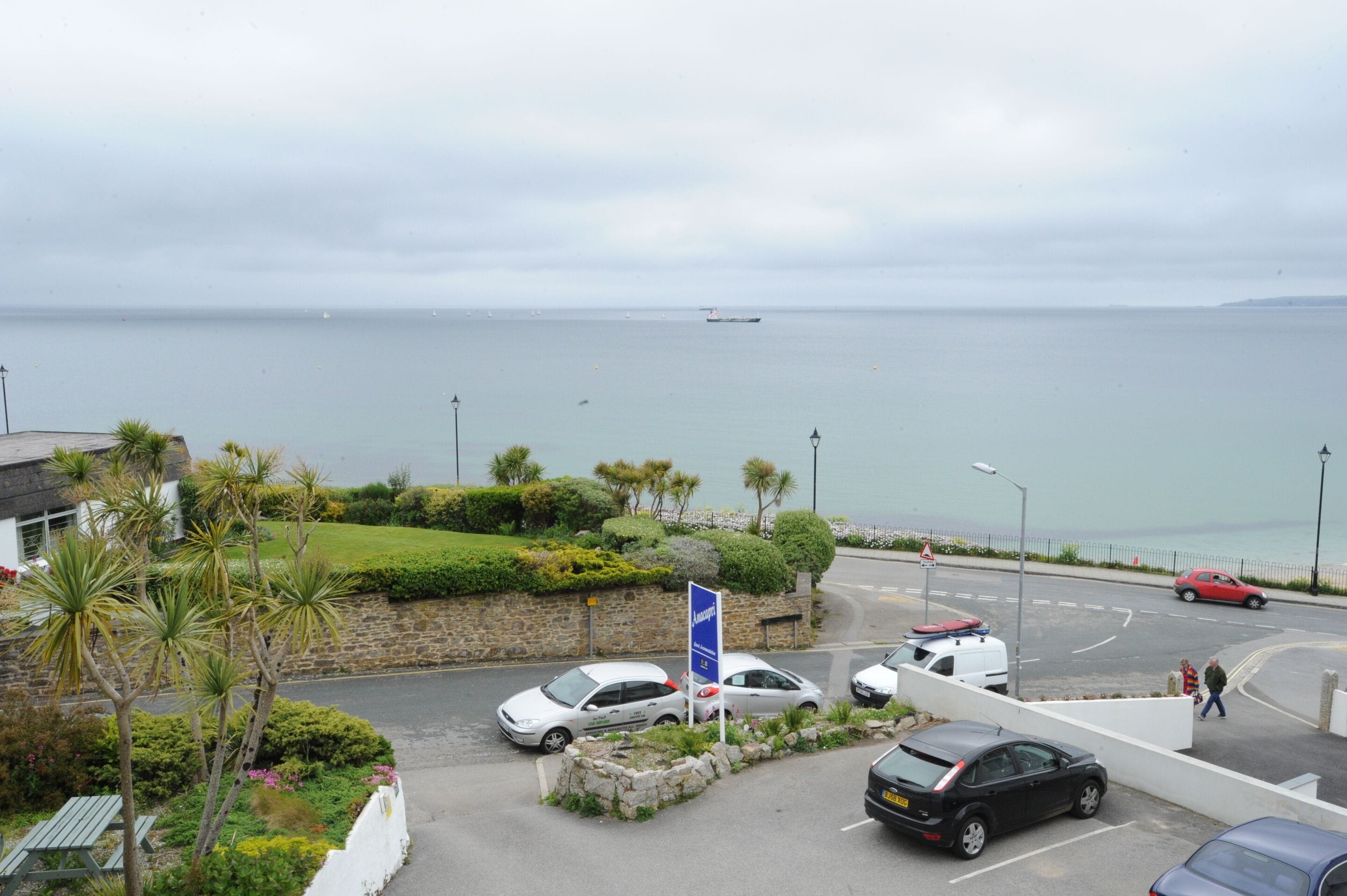 Una strada costiera con auto parcheggiate, un cartello stradale e vista sul mare.