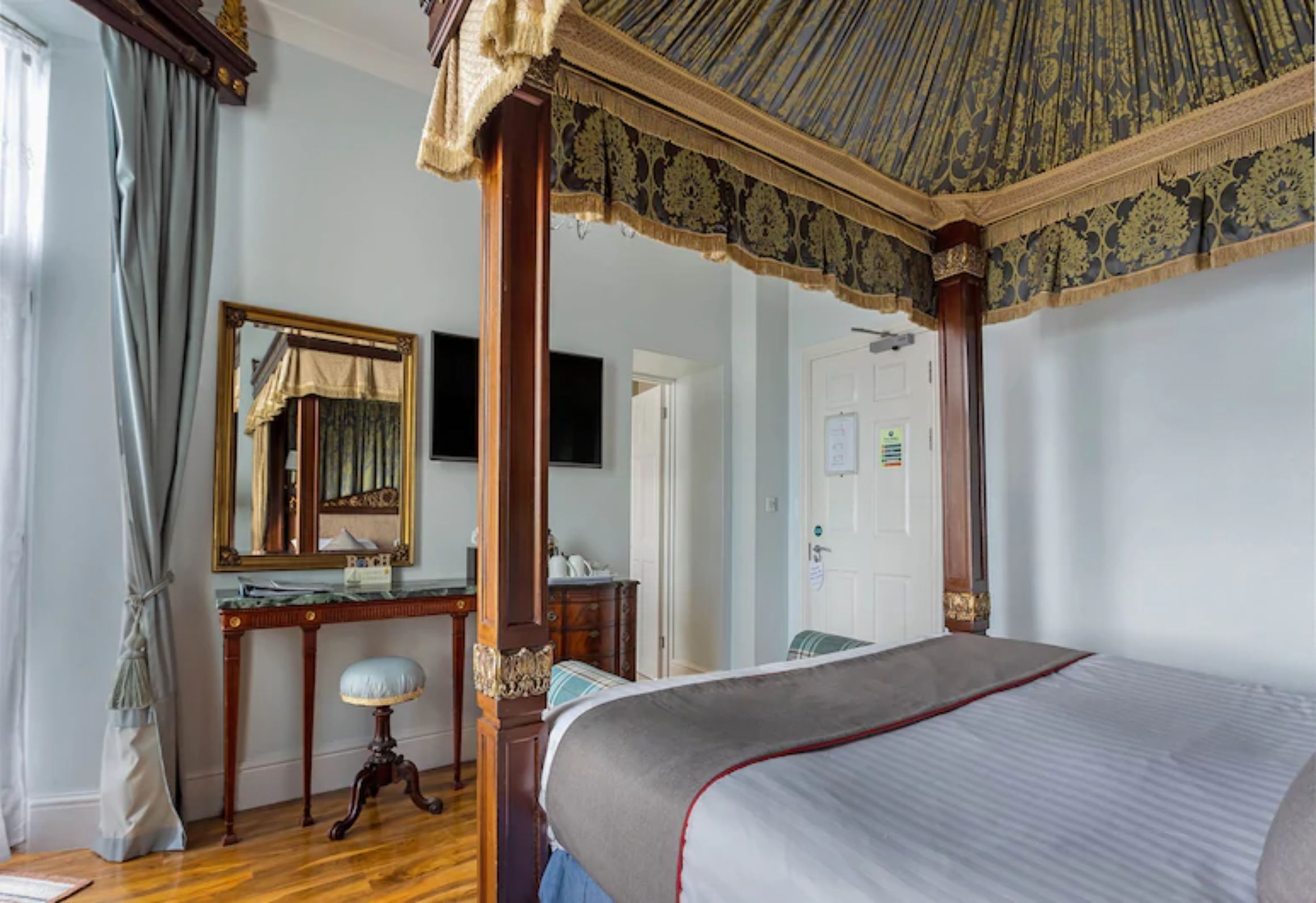 A bedroom with a four-poster bed, a wooden desk, a mirror, and a ceiling fan.