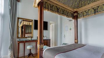 A bedroom with a four-poster bed, a wooden desk, a mirror, and a ceiling fan.