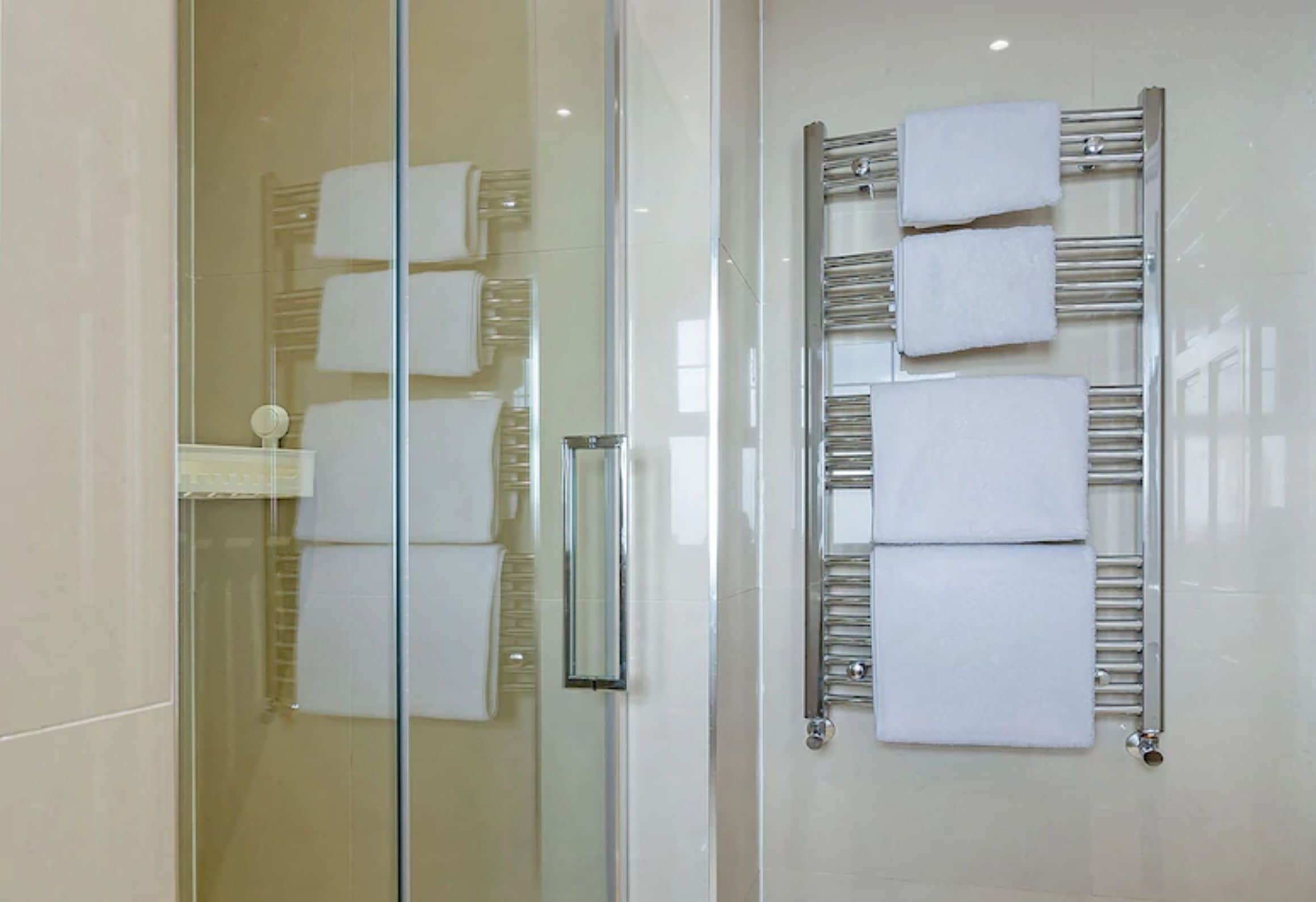 A modern bathroom with a glass shower enclosure, a glass door, and a built-in towel rack with multiple white towels.