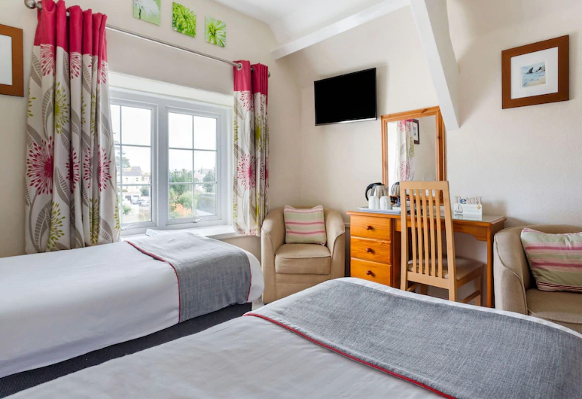 A hotel room with two beds, a desk, a chair, a television, and a window with curtains.