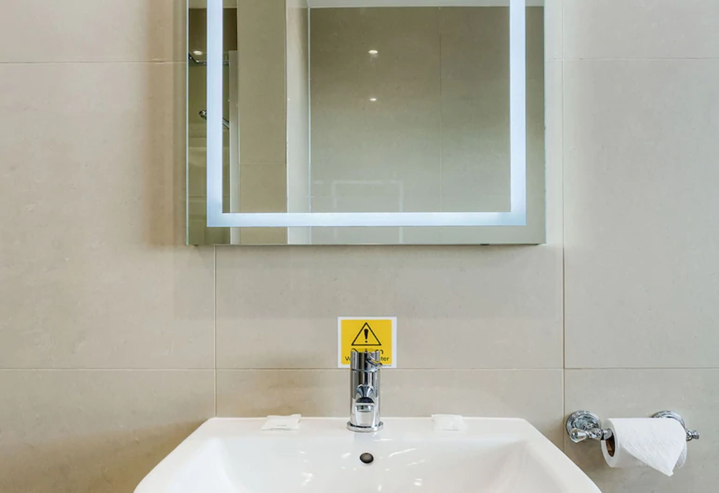 A bathroom with a white sink, a mirror, and a caution sign.